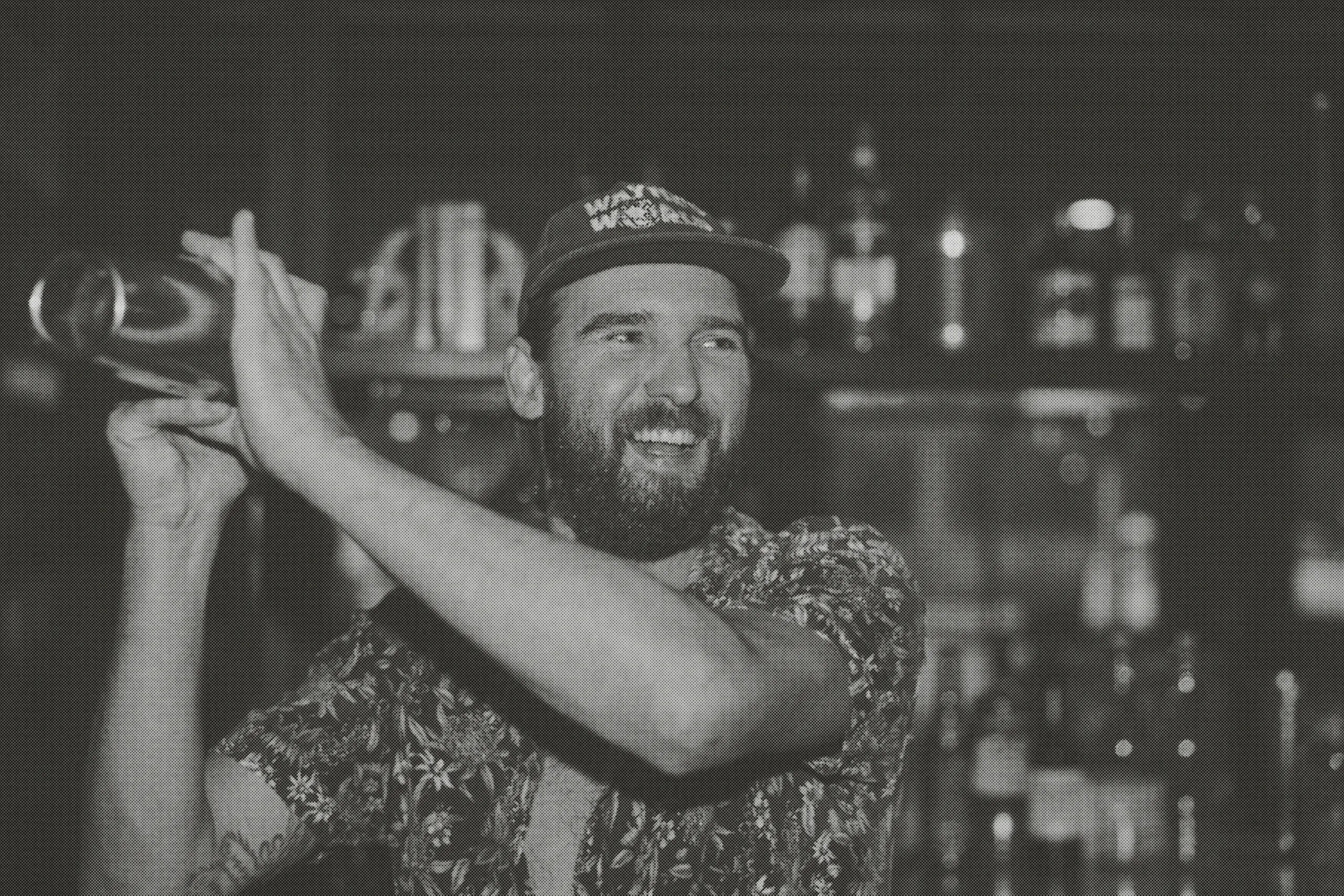 Our bartender mid-shake behind the bar, with a grin and a well-stocked shelf behind him.